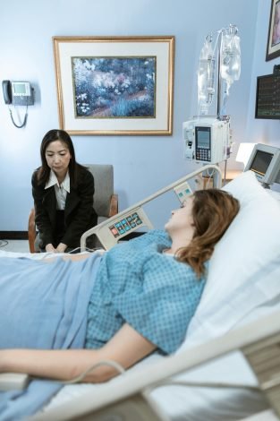 A hospital room showing a patient in bed and a visitor sitting beside her.