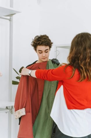 A mother assists her teenage son in selecting clothing in an indoor store setting.